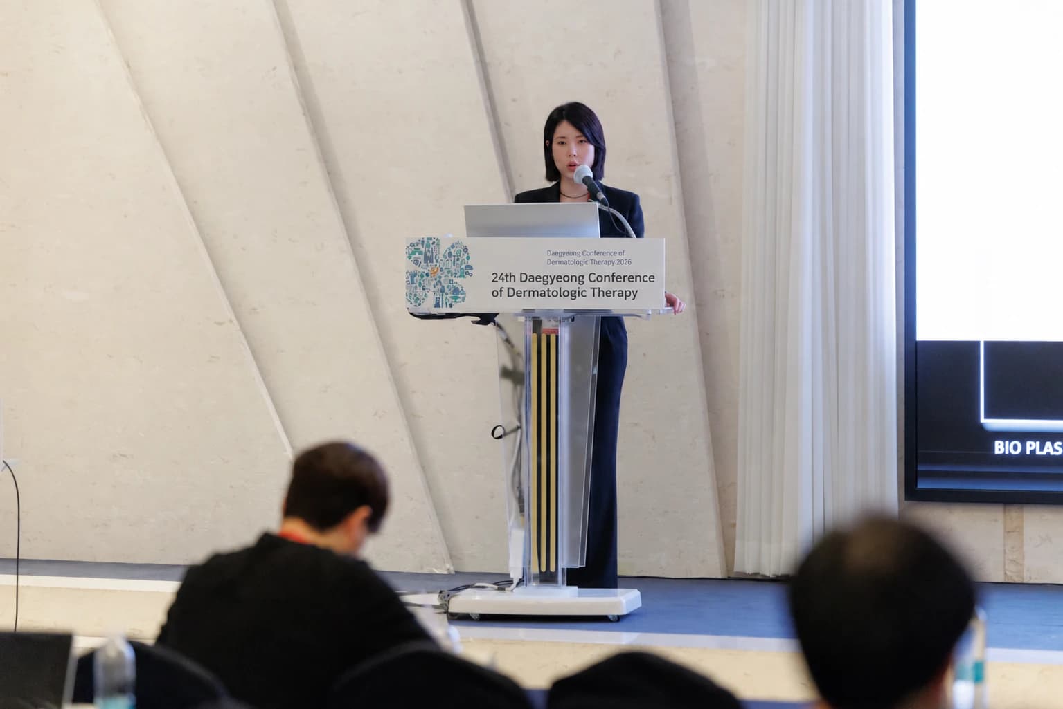 Dr. Hyemi Yu presenting at an academic conference, with the podium sign translated into English